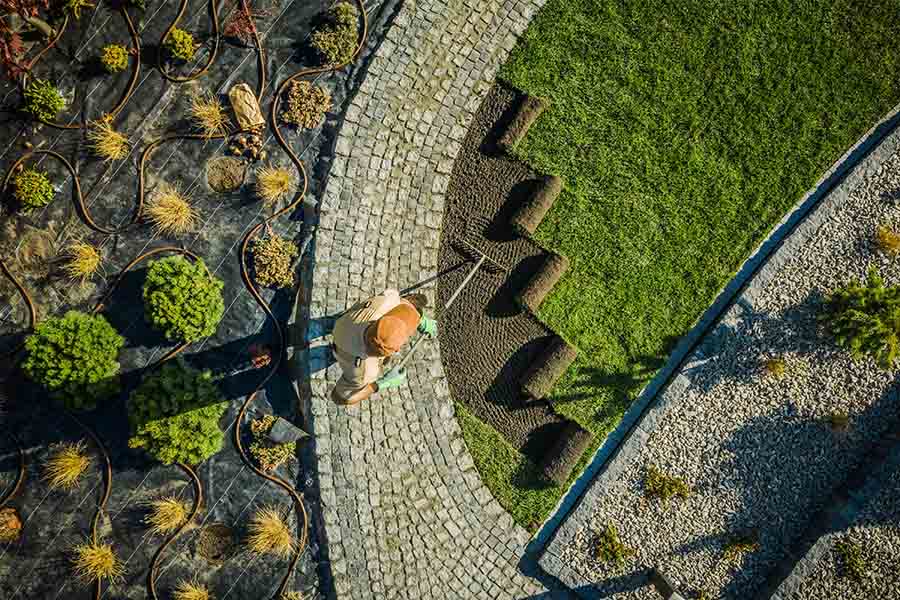 Landscaping Services Insurance - Hardworking Man Laying Down Grass Next to Garden Beds in the Late Afternoon