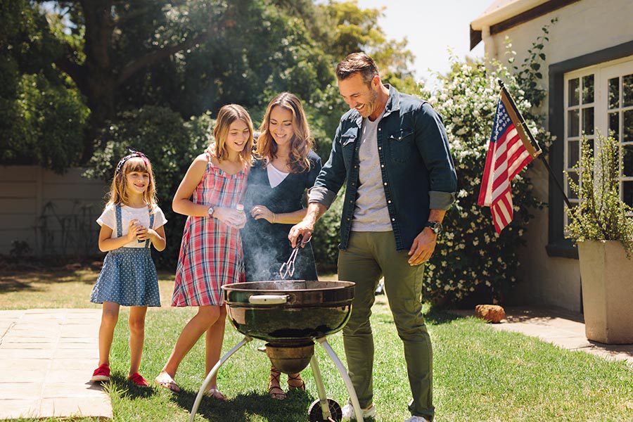 Personal Insurance - Family Barbecuing in Their Backyard on a Bright Day, American Flag on the Patio